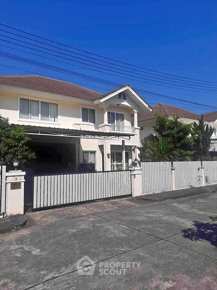 Charming two-story house with gated driveway and lush greenery under clear blue sky.