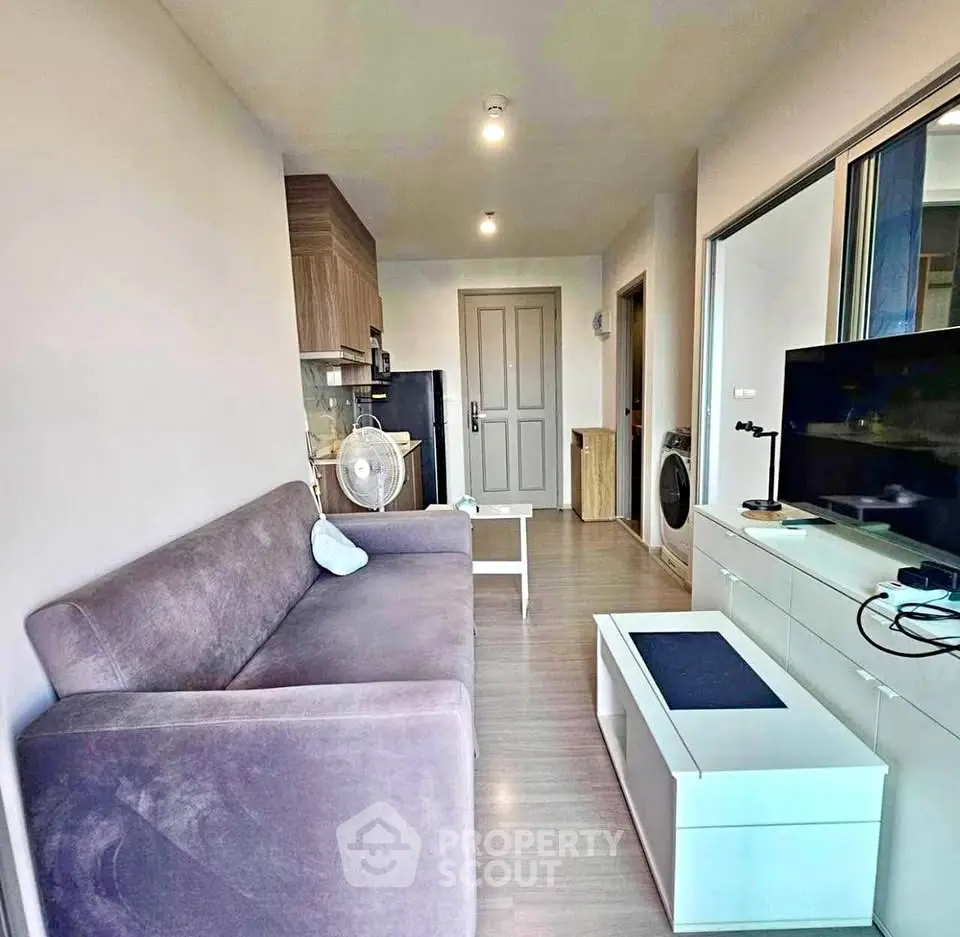 Modern living room with cozy sofa, TV unit, and compact kitchen in open layout apartment.