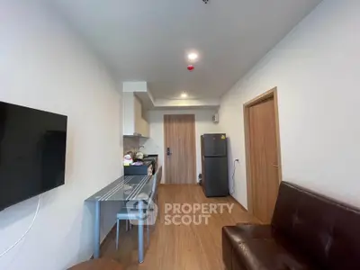 Modern apartment interior with open kitchen and cozy living area, featuring sleek furniture and wooden flooring.