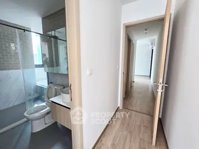 Modern apartment hallway with bathroom featuring glass shower and sleek fixtures.