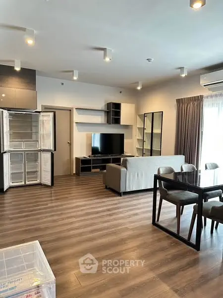 Modern living room with open kitchen, sleek furniture, and wooden flooring.