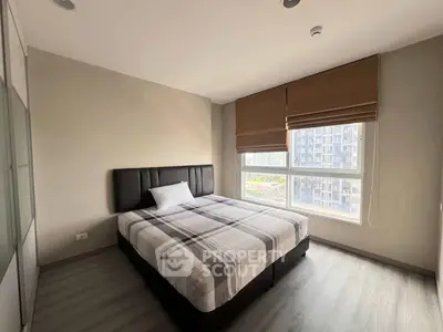 Modern bedroom with large window and stylish decor in urban apartment.