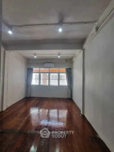 Spacious room with polished wooden floors and large windows, ideal for versatile living space.