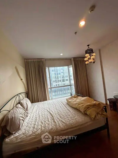 Spacious bedroom with large window offering city view, featuring elegant lighting and cozy bedding.