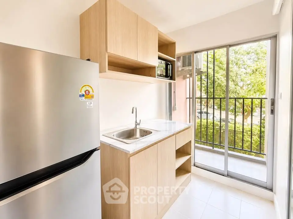 Modern kitchen with sleek cabinetry and stainless steel fridge, featuring a bright view through sliding glass doors.