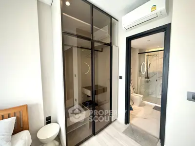 Modern bedroom with glass wardrobe and ensuite bathroom in stylish apartment.
