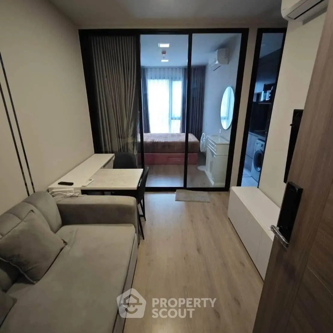 Modern apartment interior with cozy living room and bedroom separated by glass wall.