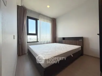Spacious bedroom with large window and modern furnishings in high-rise apartment.