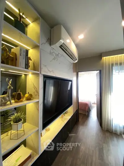 Modern living room with stylish shelving and large TV, leading to a cozy bedroom.