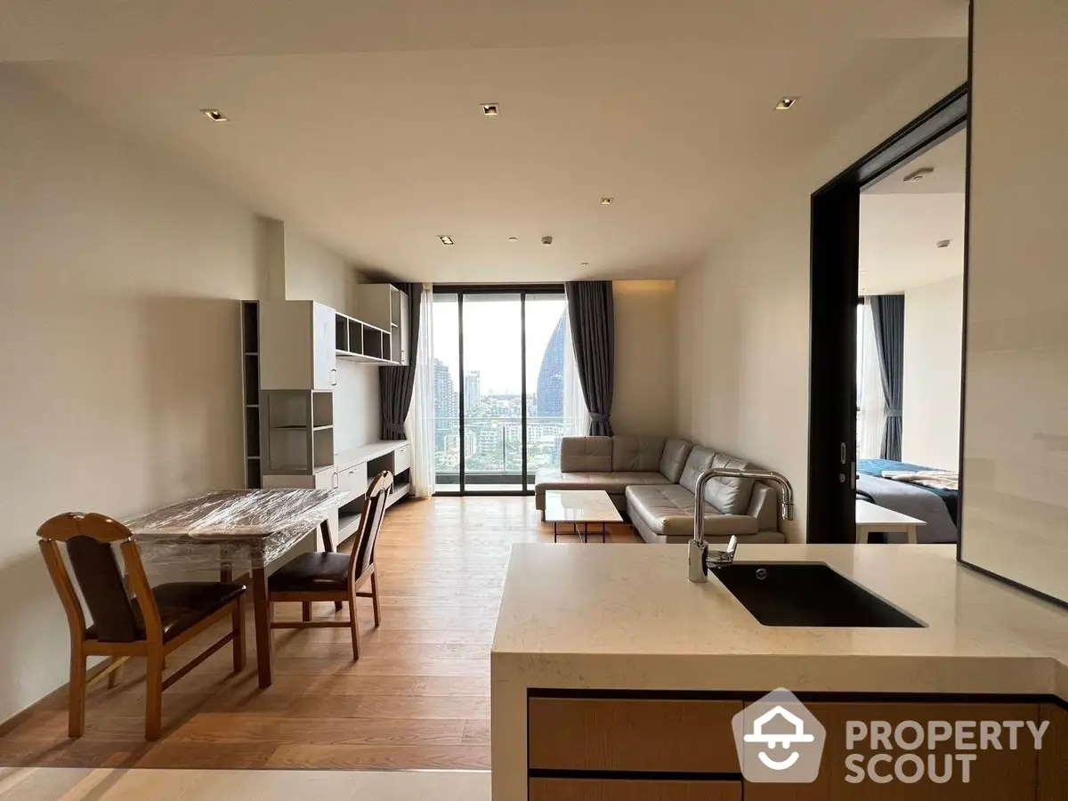 Spacious open-plan living area with modern kitchen, ample natural light, and sleek furnishings leading to a large balcony with city views.