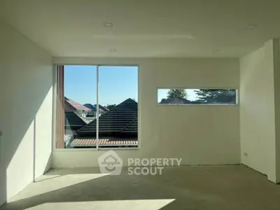 Spacious empty room with large windows offering a scenic view of rooftops and clear skies.