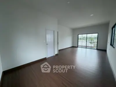 Spacious empty room with wooden flooring and large window leading to a balcony, perfect for customization.