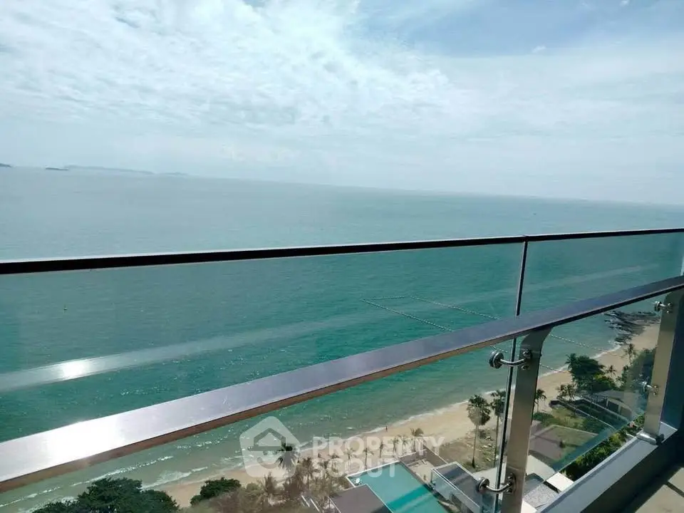 Stunning ocean view from a high-rise balcony overlooking a pristine beach and clear blue waters.