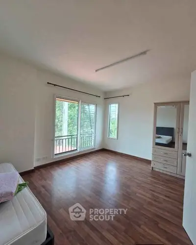 Spacious bedroom with wooden flooring and large windows offering natural light and greenery views.