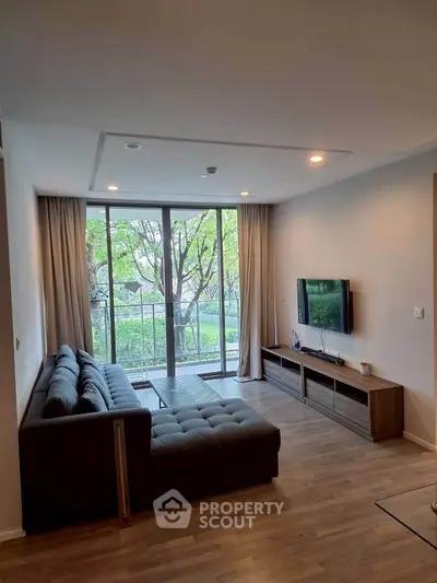Modern living room with large window and stylish furniture overlooking lush greenery.