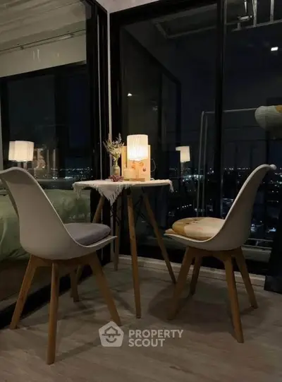 Cozy balcony dining area with city night view, featuring modern chairs and ambient lighting.