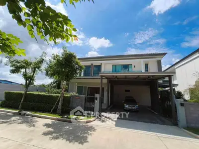 Modern two-story house with carport and lush greenery under a clear blue sky.