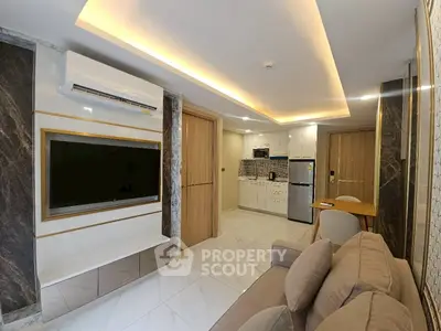 Modern living room with sleek design, featuring a large TV, air conditioning, and a compact kitchen area.