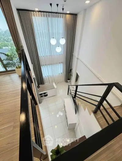 Stunning duplex interior with high ceilings and modern staircase, featuring elegant lighting and large windows.