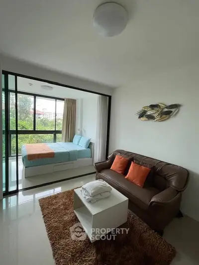 Modern studio apartment with cozy living area and large windows offering a lush green view.