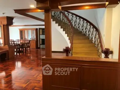 Elegant wooden staircase in a spacious living area with dining set and polished floors.