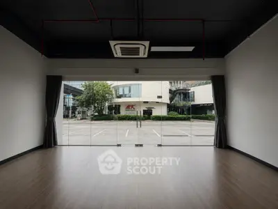 Spacious empty room with large glass windows offering a view of the cityscape, ideal for commercial use.