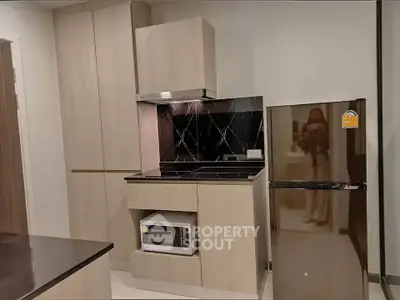 Modern kitchen with sleek cabinetry, microwave, and fridge in stylish apartment.