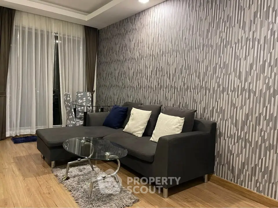 Modern living room with stylish gray sofa and glass coffee table, featuring elegant wallpaper and wooden flooring.