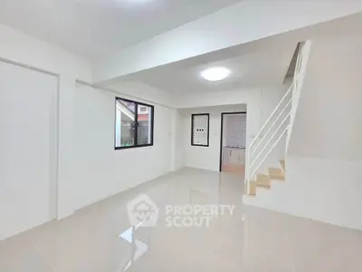 Spacious modern living room with sleek staircase and large windows in a contemporary home.