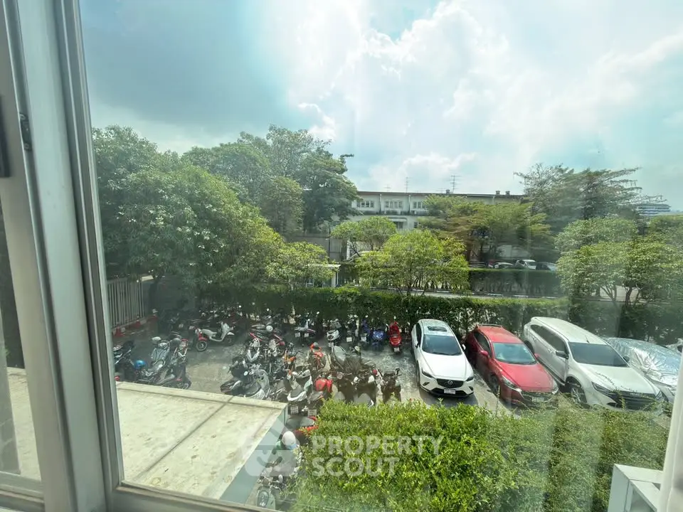 Scenic view from window overlooking parking area with lush greenery and parked vehicles.