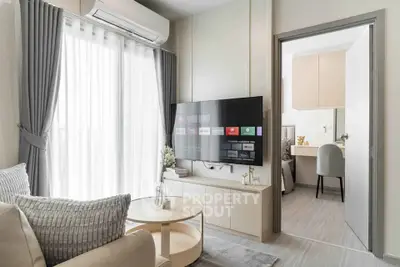 Modern living room with sleek design, featuring a wall-mounted TV, cozy seating, and natural light from large windows.