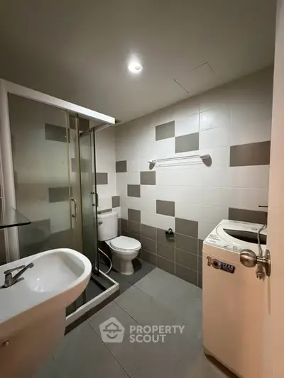 Modern bathroom with shower, washing machine, and stylish tile design.