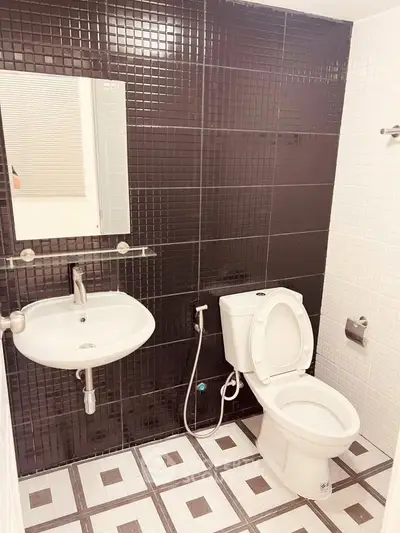Modern bathroom with sleek black and white tile design, featuring a wall-mounted sink and toilet.