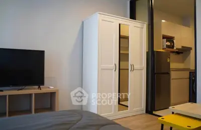 Modern studio apartment with sleek kitchen and cozy living area, featuring a wardrobe and flat-screen TV.