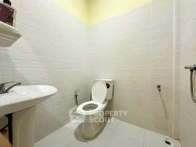 Spacious bathroom with modern white tiles and essential fixtures.