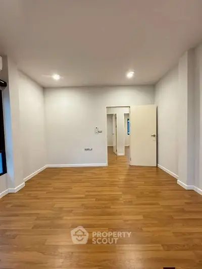 Spacious empty room with wooden flooring and white walls, ideal for customization.