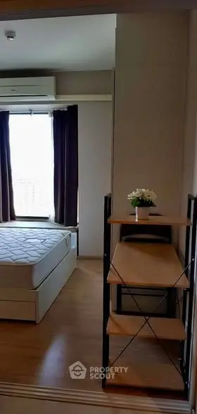 Cozy bedroom with wooden flooring and natural light, featuring a bed and a small desk with a plant.