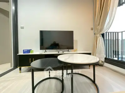 Modern living room with sleek TV setup and stylish round tables near a balcony view.
