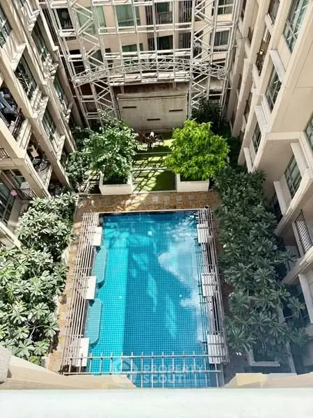 Stunning aerial view of luxury apartment pool surrounded by lush greenery and modern architecture.