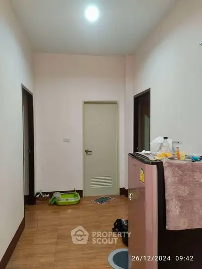 Compact hallway with wooden flooring and minimal decor, featuring a small refrigerator and basic furnishings.