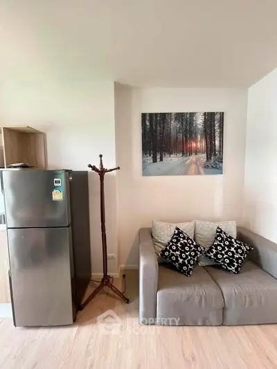 Modern living room with cozy sofa and stylish decor, featuring a sleek refrigerator and scenic wall art.