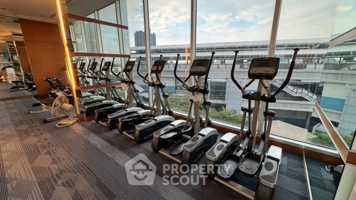 Modern gym with elliptical machines and city view through large windows.