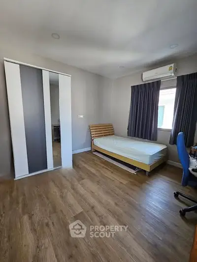 Spacious bedroom with wooden flooring and modern furniture, featuring a single bed and large wardrobe.