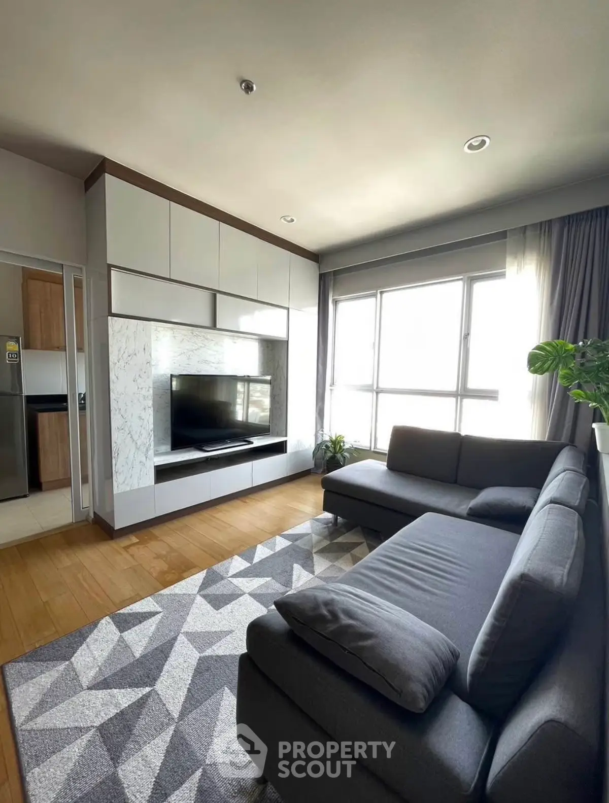 Stylish modern living room with cozy gray sofas and large TV, featuring natural light and elegant decor.