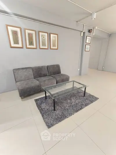 Modern living room with sleek gray sofa and glass coffee table on plush rug.