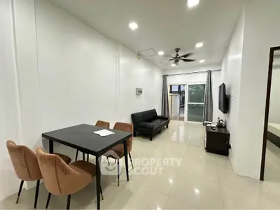 Modern living room with sleek furniture and dining area, featuring a ceiling fan and natural light.