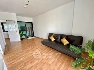 Spacious living room with modern decor and wooden flooring, featuring a sleek black sofa and decorative plants.