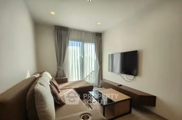 Modern living room with sleek furniture and wall-mounted TV, featuring natural light through large windows.