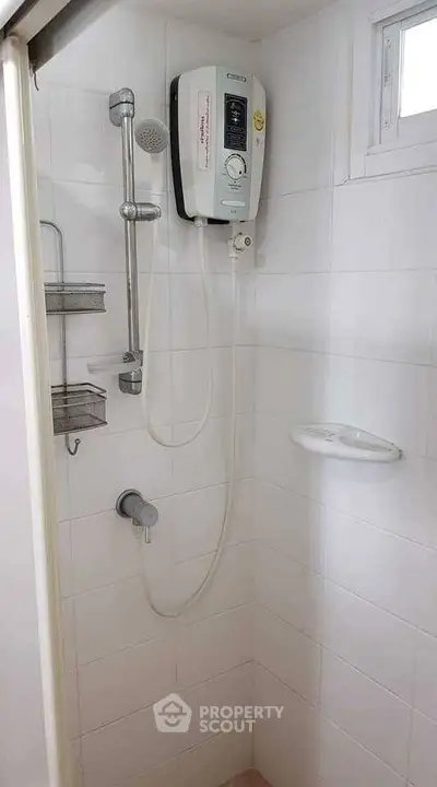 Compact bathroom shower area with electric water heater and white tiles.