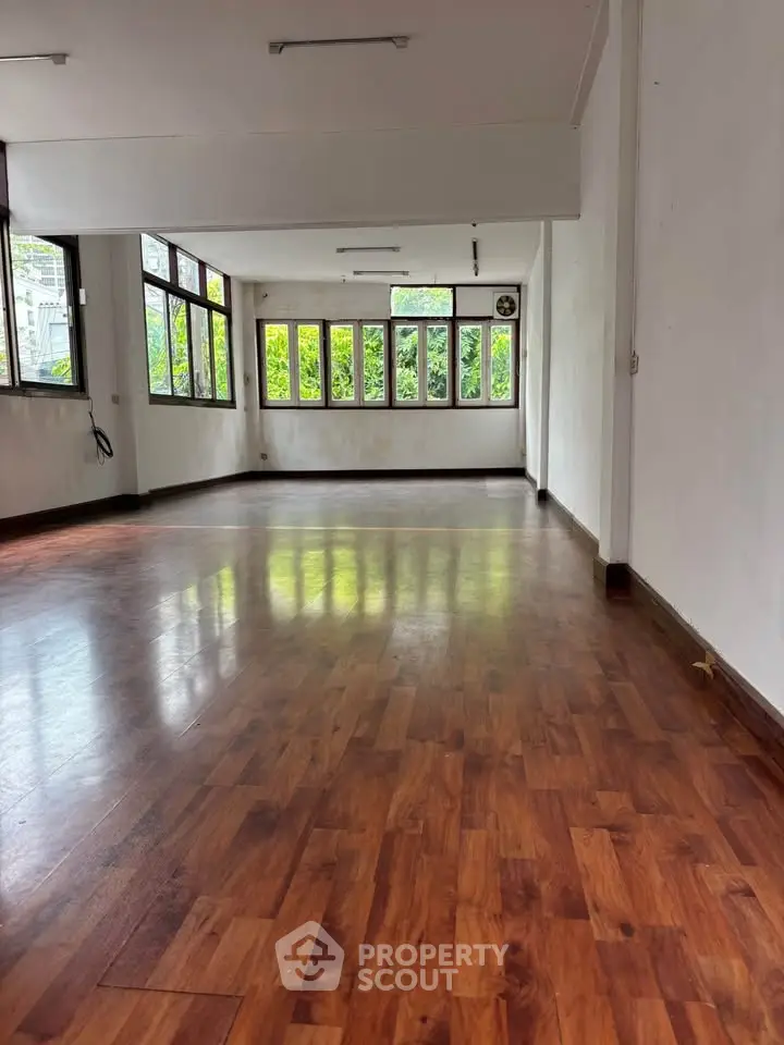 Spacious empty room with wooden flooring and large windows offering natural light.